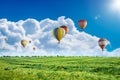 Multicolored hot air balloons fly in blue sky with white clouds over green field Royalty Free Stock Photo