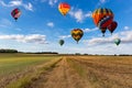 Multicolored hot air balloons fly in blue sky with white clouds over green field Royalty Free Stock Photo