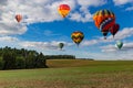 Multicolored hot air balloons fly in blue sky with white clouds over green field Royalty Free Stock Photo