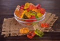 Multicolored jelly bears in a glass bowl on a dark wooden background.