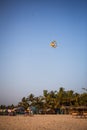 A multicolored kite flies over a large sandy beach in Kerala, India.