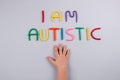 Multicolored letters, I am Autistic - on light gray background with child hand. World Autism Awareness Day, Autism