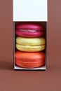 Multicolored macarons in a cardboard box with an open lid standing upright on a brown background. Closeup Royalty Free Stock Photo