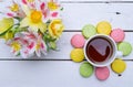 Multicolored macaroons, flowers and cup of hot tea on a wooden t Royalty Free Stock Photo