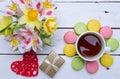 Multicolored macaroons, flowers, a gift and a cup of hot tea on