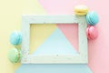 Multicolored macaroons on pastel geometric background and vintage empty frame.