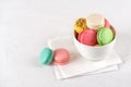 Multicolored macaroons in a white ceramic bowl on a light background. Colorful macaron cakes variety. Delicious french dessert.