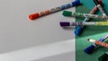 Multicolored markers lie on the background of colored cardboard and white paper close-up
