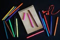 Multicolored markers, notebook made of eco-friendly paper and red in-ear headphones - earbuds lie on black background. The concept Royalty Free Stock Photo