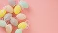 Multicolored pastel decorative eggs on the left on a pink background. Copy space.