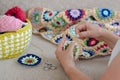 Multicolored plaid squares of crocheted on a cream colored seat and woman is crocheting Royalty Free Stock Photo