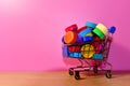 Multicolored Plastic bottle caps in shopping trolley on pink background. Cap material is recyclable. Lids from plastic bottles ror