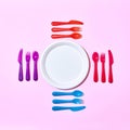 Multicolored plastic utensil around white plate on a light pink. Royalty Free Stock Photo