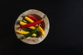 Multicolored pods of hot chili peppers lie on a wooden textured plate tray bowl on a black background with copy space Royalty Free Stock Photo