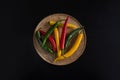 Multicolored pods of hot chili peppers lie on a wooden textured plate tray bowl on a black background with copy space Royalty Free Stock Photo