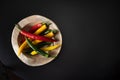 Multicolored pods of hot chili peppers lie on a wooden textured plate tray bowl on a black table Royalty Free Stock Photo