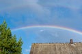 Multicolored rainbow over the roof of the house against the blue sky with clouds Royalty Free Stock Photo