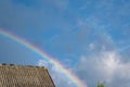 Multicolored rainbow over the roof of the house against the blue sky with clouds Royalty Free Stock Photo