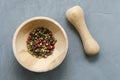 Multicolored red green black peppercorns in a wooden mortar with a pestle on a gray concrete background close-up with a place for Royalty Free Stock Photo