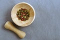 Multicolored red green black peppercorns in a wooden mortar with a pestle on a gray concrete background close-up with a Royalty Free Stock Photo