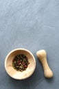 Multicolored red green black peppercorns in a wooden mortar with a pestle on a gray concrete background close-up with a