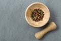 Multicolored red green black peppercorns in a wooden mortar with a pestle on a gray concrete background close-up with a place for Royalty Free Stock Photo