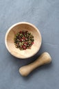 Multicolored red green black peppercorns in a wooden mortar with a pestle on a gray concrete background close-up with a Royalty Free Stock Photo