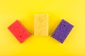 Close up of three multicolored red, purple and yellow cleaning sponges on bright yellow background