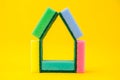 Multicolored sponges for cleaning folded in the shape of a house on a yellow background. Space for text