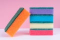 Multicolored sponges for washing dishes on top of each other on a pink background. Cleaning concept