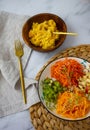 multicolored vegetable salad on a white plate and yellow millet porridge in a wooden bowl vertically