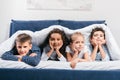 multicultural children looking at camera while lying together in bed Royalty Free Stock Photo