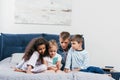 multicultural children sitting on bed together and using smartphone Royalty Free Stock Photo