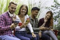 Multicultural friends having fun together looking at their smartphones  at dehor garden on college campus - People addicted by Royalty Free Stock Photo