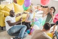 multicultural friends in party hats sitting on floor with balloons in decorated