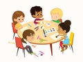 Multicultural, multi aged boys and girls sit at a round table playing games, make applique and painting. Kids draw