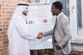 Multiethnic businessmen shaking hands near white board