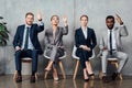 Multiethnic businesspeople sitting on chairs with raised hands ready to answer in