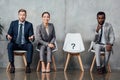 Multiethnic businesspeople sitting near card with question mark on chair in waiting hall and looking Royalty Free Stock Photo