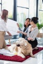 Multiethnic businesswomen looking at blueprint with dog at office
