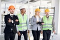 Multiethnic four male and female architects and engineers in hardhats inspecting unfinished office building