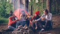 multiethnic group of friends girls and guys are sitting in forest around fire with drinks clinking glasses and smiling Royalty Free Stock Photo