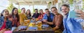 Multiethnic large group of friends sitting on a table in a bar restaurant making a selfie portrait. diverse people celerating