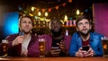 Multiethnic male friends watching football match in pub, upset with team losing