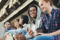 Multiethnic teen friends sitting outdoors, talking and using gadgets