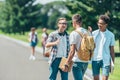 multiethnic teenage boys with books and backpacks talking and smiling each other