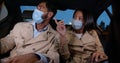 Multiethnic young couple in safety mask sitting on backseat in car