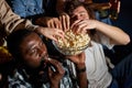 multiethnic young friends watch film together at home at night, eating snacks