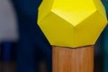 The multifaceted yellow figure is made of many yellow paper pentagons on a wooden stand