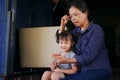 Multigeneration togetherness in Asian family, little girl watching smart phone and listening story tale with grandmother in